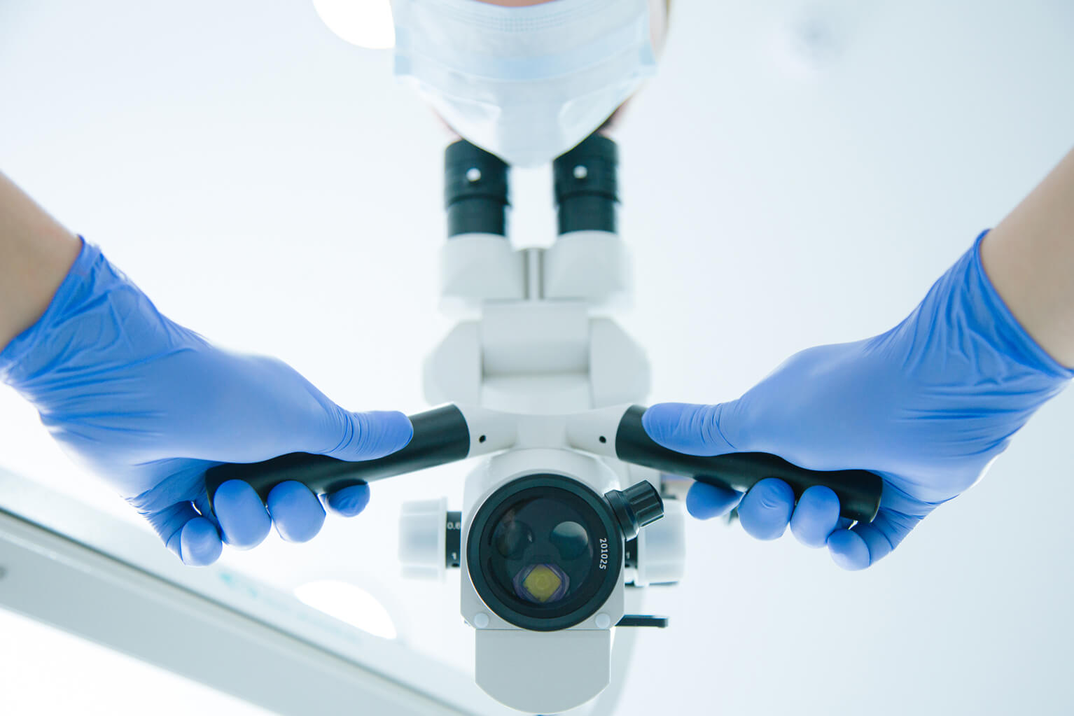 Close up of medical worker in blue rubber gloves putting hands on the operating microscope handles